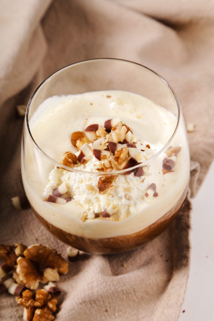 Creamy almond milk rice pudding topped with chopped nuts and whipped cream in a glass cup, served on a neutral cloth background.