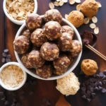 A variety of homemade energy balls on a rustic wooden board, made with oats, dates, nut butter, and coconut.
